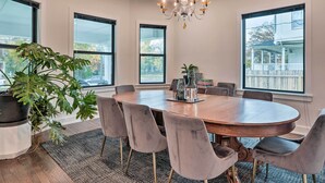 A dining area with a round wooden table, six chairs, a chandelier, and large windows. - Grand Long Branch Home: 1 Block to Beach! (Long Branch)