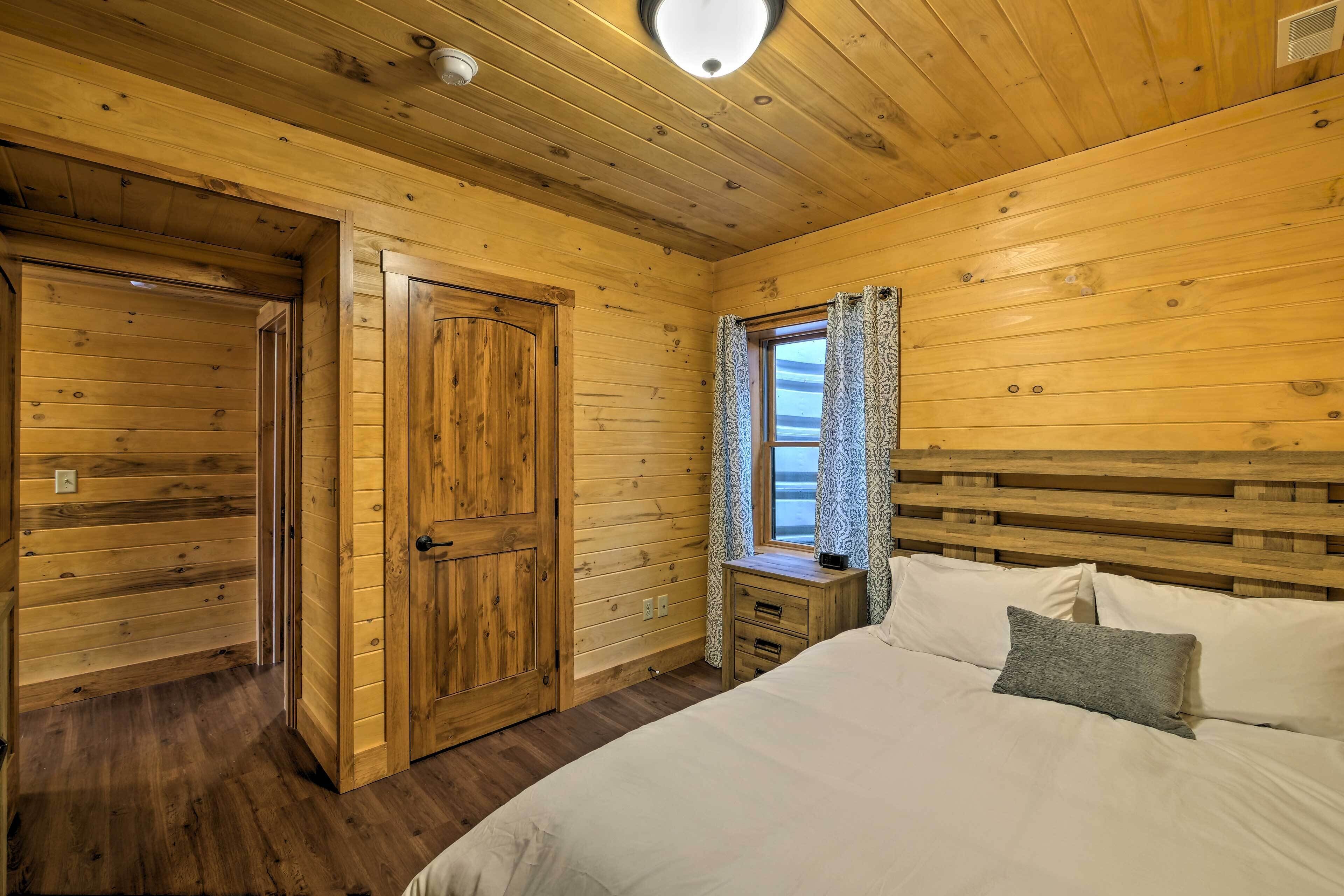Una camera da letto in una baita di legno, con un letto, un comodino, una finestra con tende e una porta in legno.