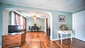 A room with wooden flooring, a ceiling fan, a TV on a wooden dresser, a dining table with chairs, and a white side table with drawers. - Eastlake Home w/ Patio < 1 Mi to Lake Erie! (Eastlake)