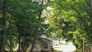 A secluded cabin surrounded by dense trees, a pathway leading to it, and a parked vehicle in the background. - Eastlake Home w/ Patio < 1 Mi to Lake Erie! (Eastlake)