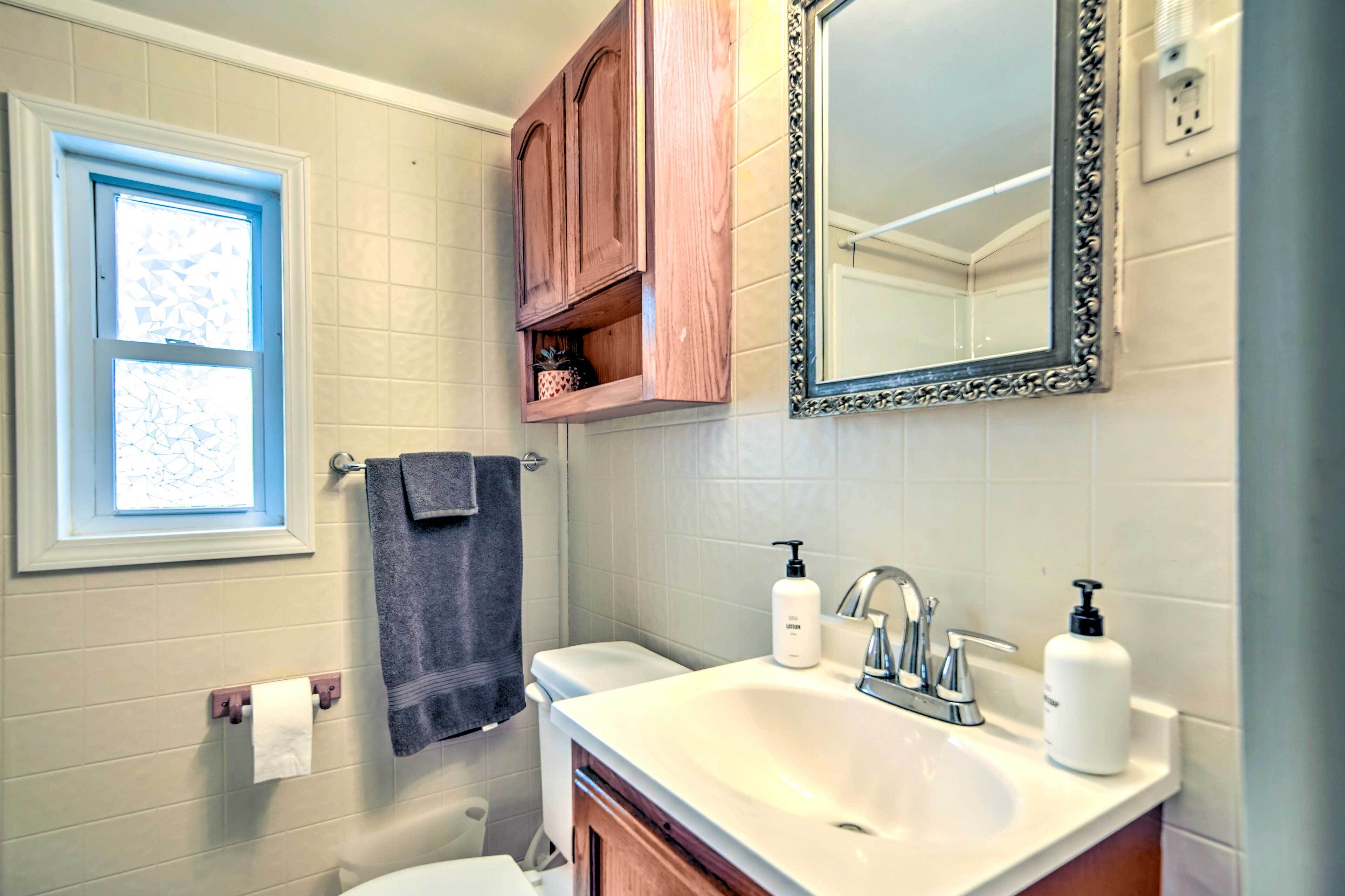 A bathroom with a white sink, a mirror with an ornate frame, a window with blue trim, and wooden cabinets above the sink.