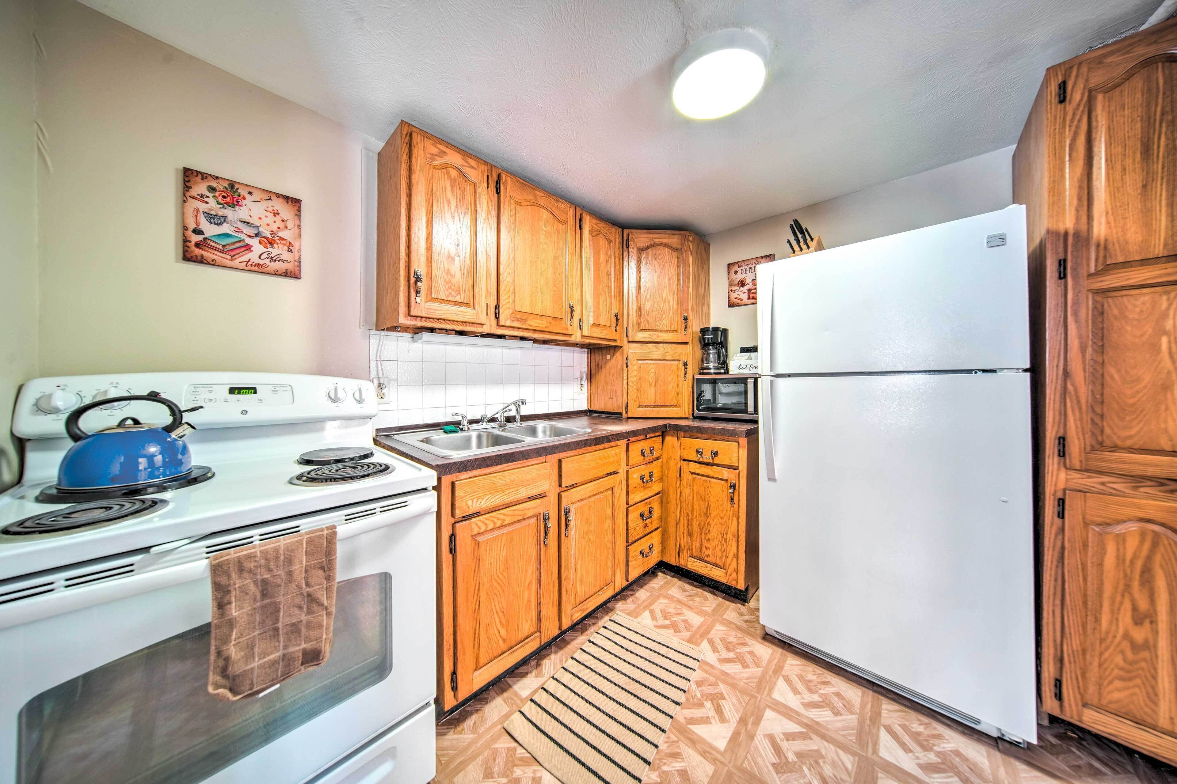 A compact kitchen with wooden cabinets, a white stove, a sink, and a refrigerator.