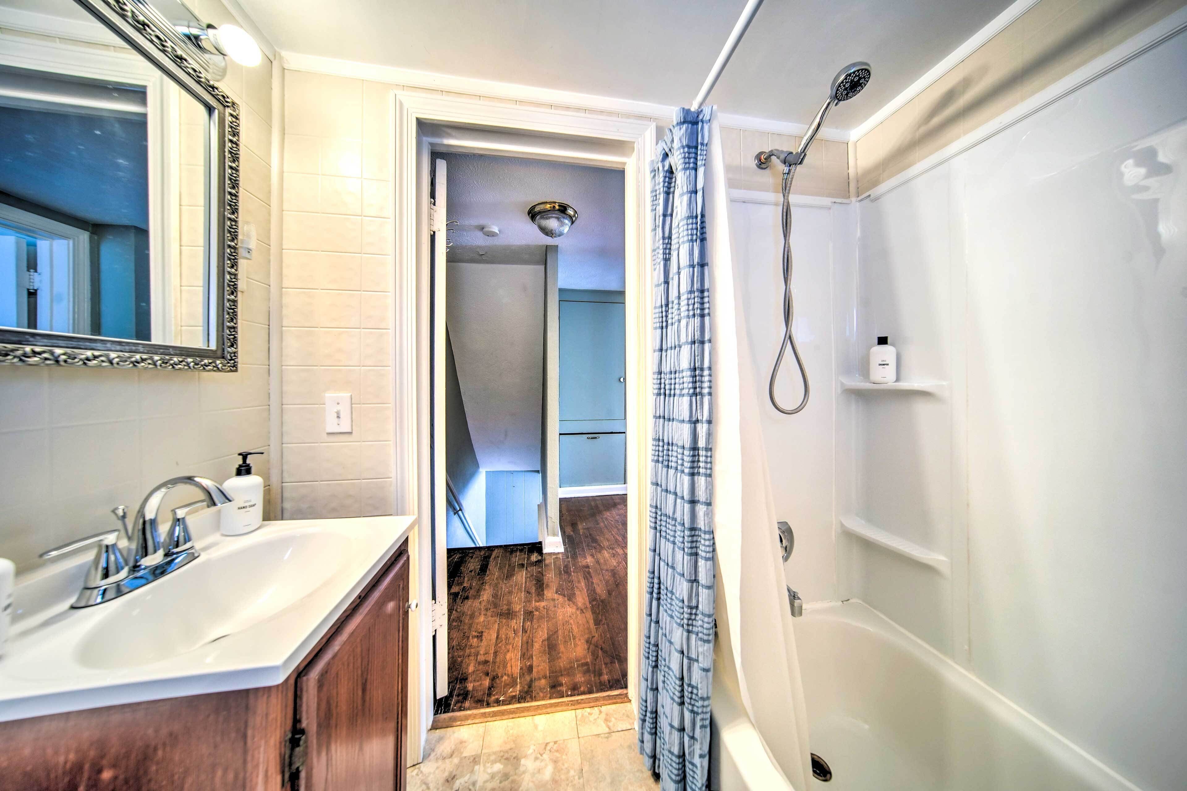 A bathroom with a sink, mirror, shower, and a door leading to another room.