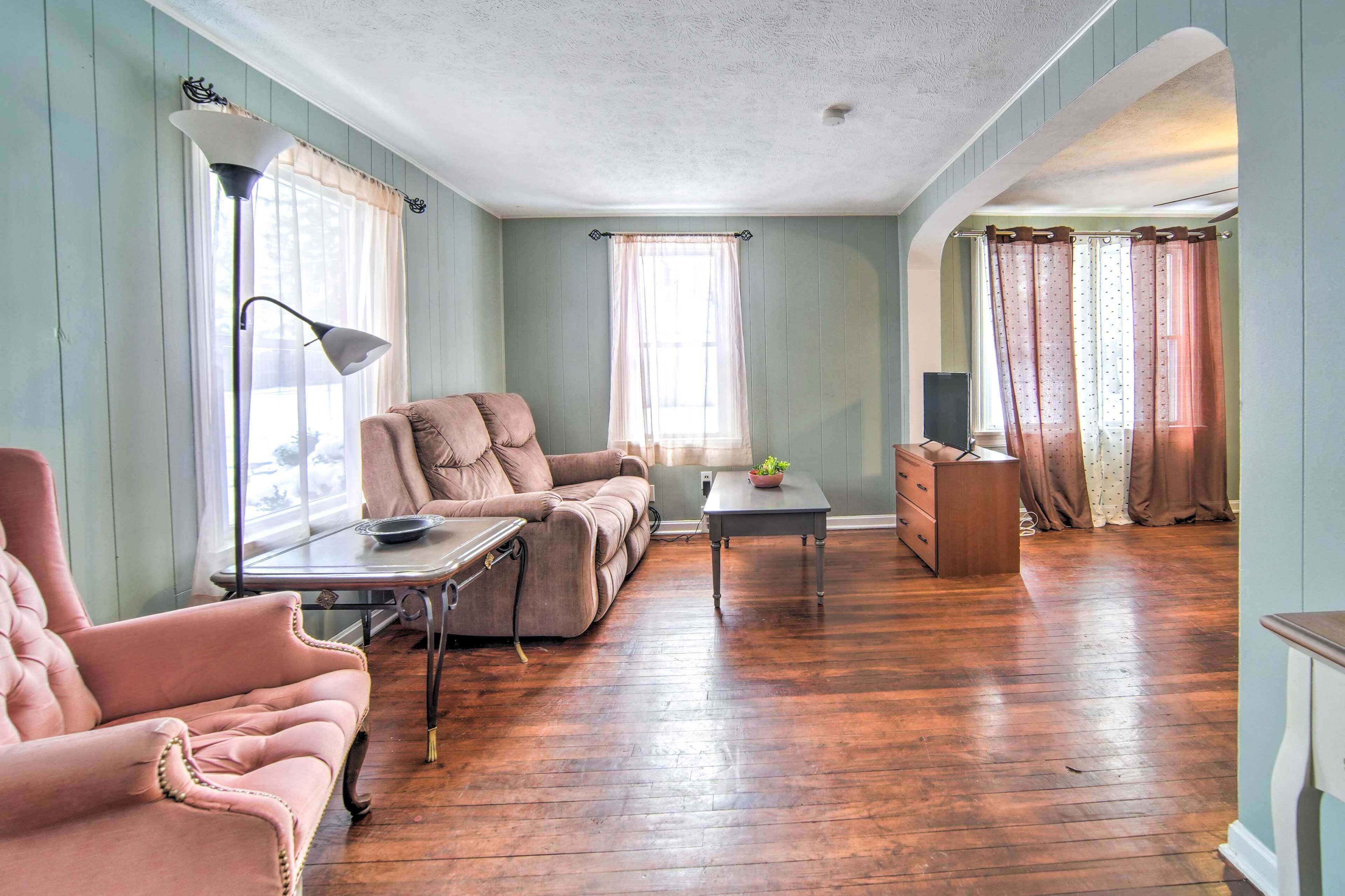 A spacious living room with a wooden floor, a sofa, a chair, a table, and a lamp.