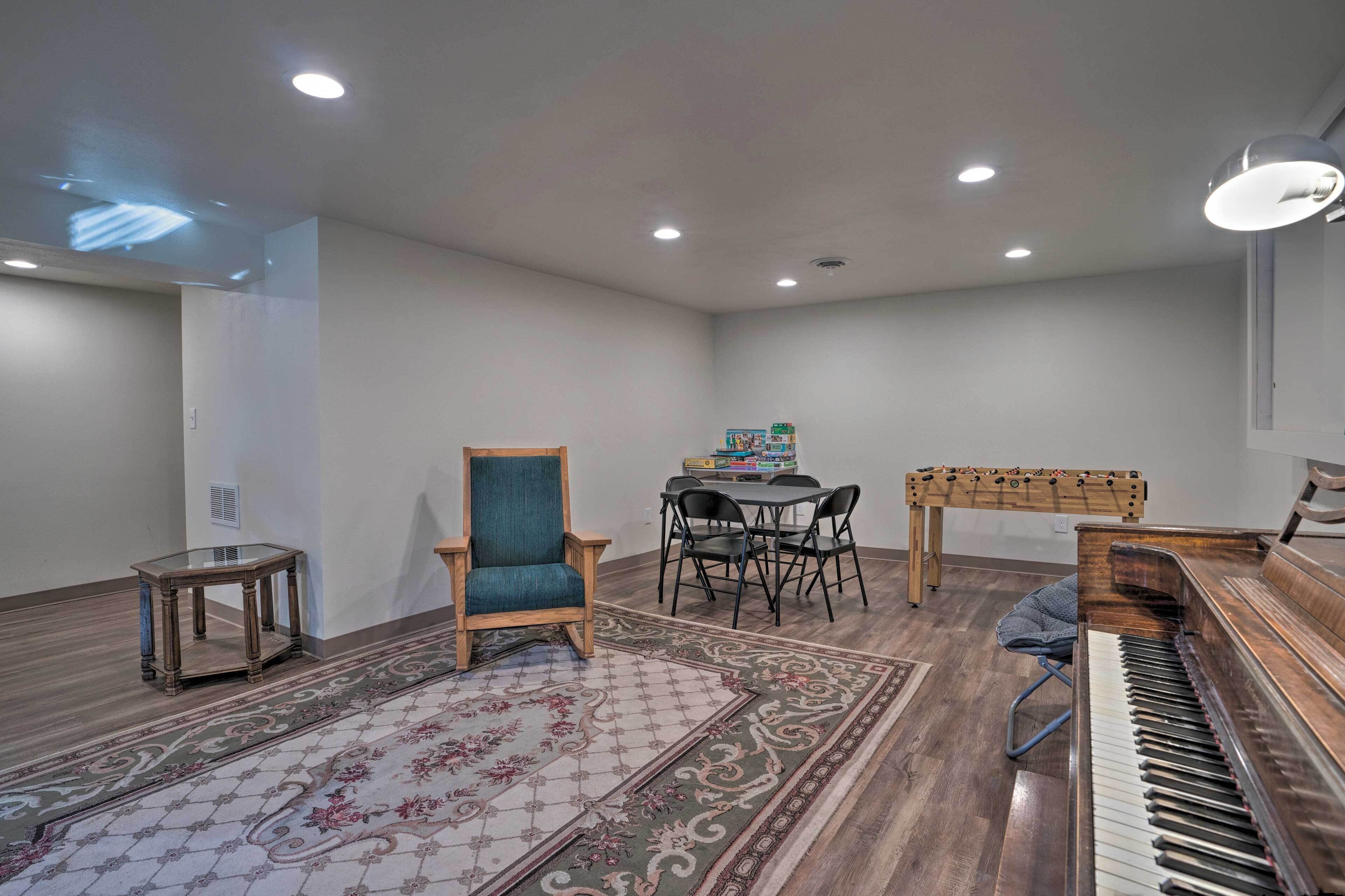 A room with a piano, a wooden chair, a table with chairs, and a foosball table.