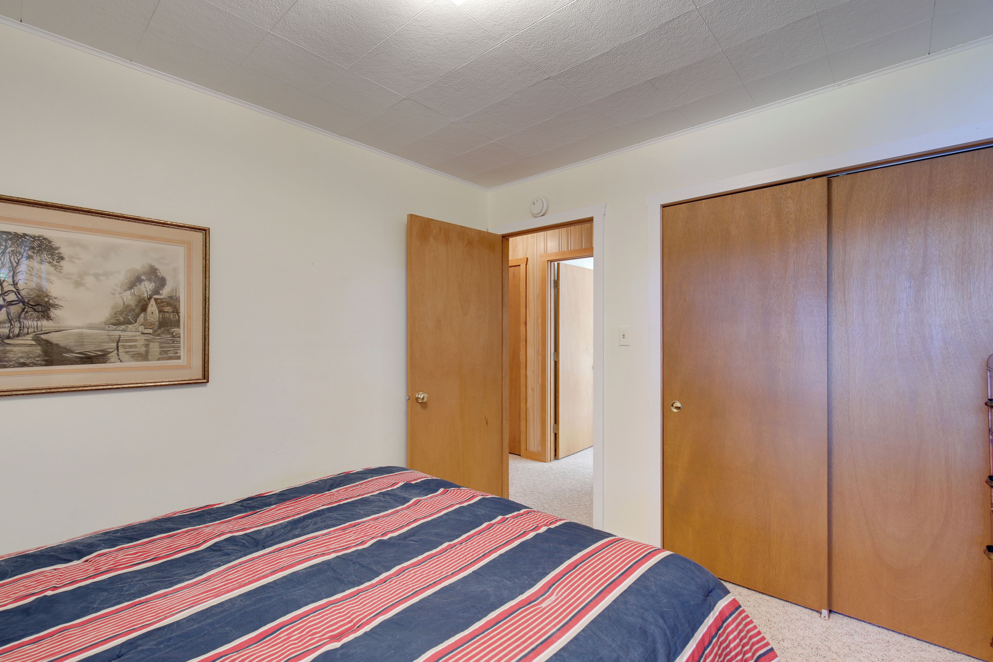 A bedroom with a bed, a wooden wardrobe, and a framed picture on the wall.