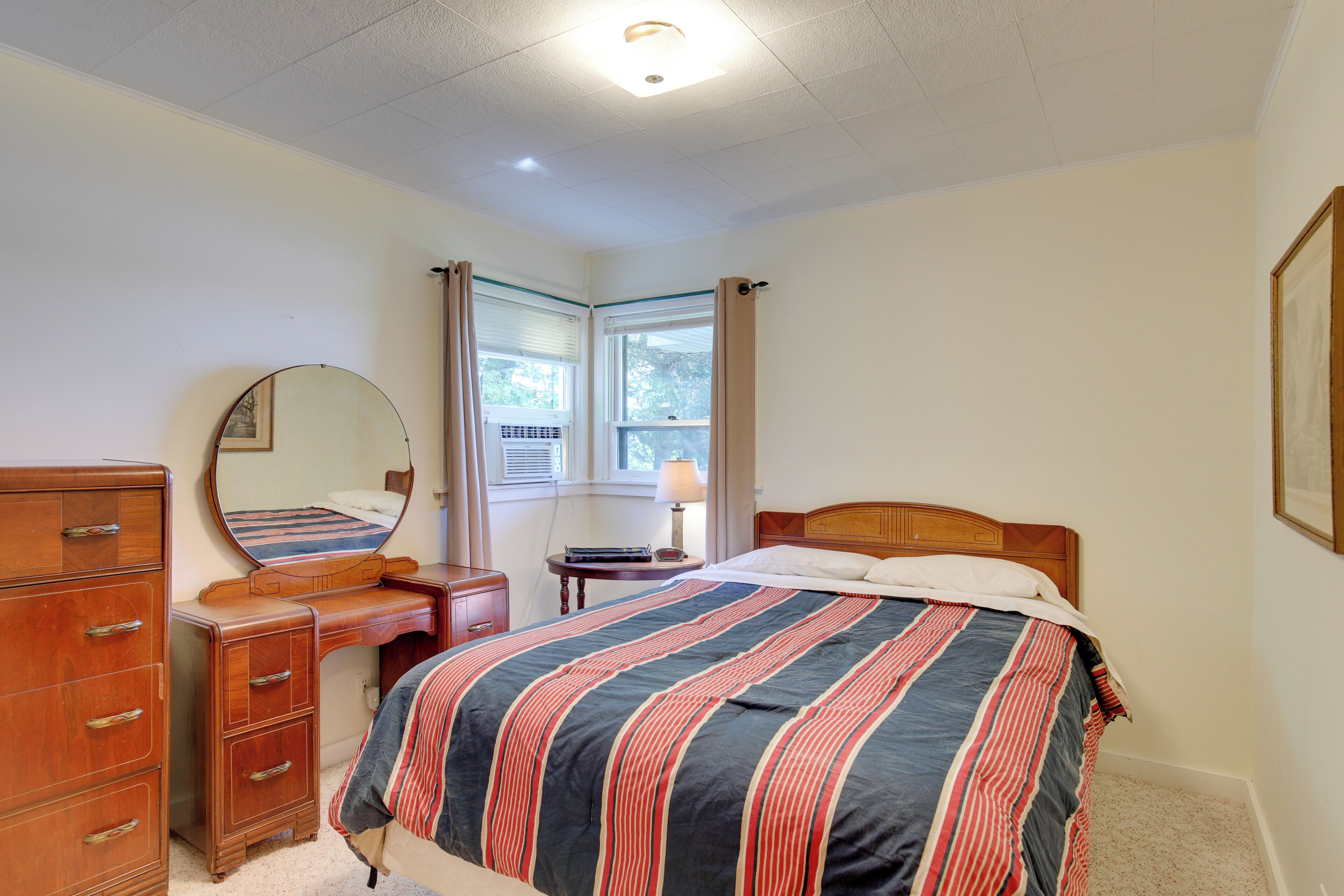 A bedroom with a bed, dresser, mirror, and window with curtains.