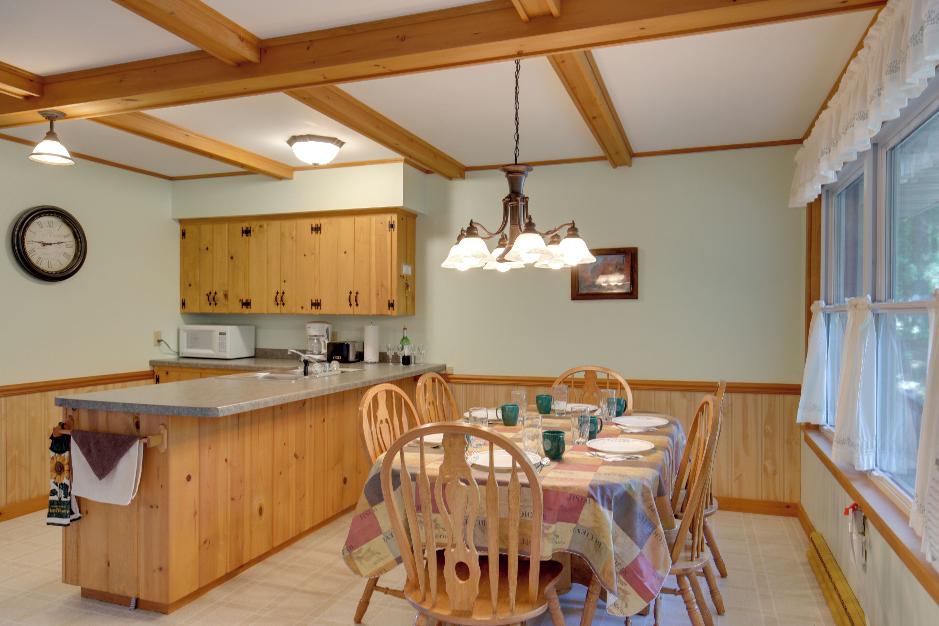 A kitchen with wooden cabinets, a central island, and a dining area with wooden chairs and a table set for four.