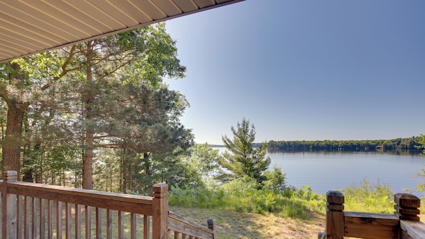 Una terraza de madera con vista a un lago, árboles y un cielo despejado.