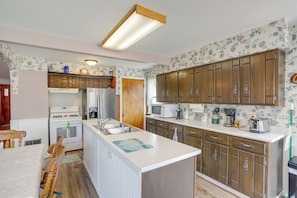 A kitchen with wooden cabinets, a central island, a refrigerator, a microwave, and a stove. - Home w/ Screened-in Porch < 1 Mi to Lake Erie (Port Clinton)
