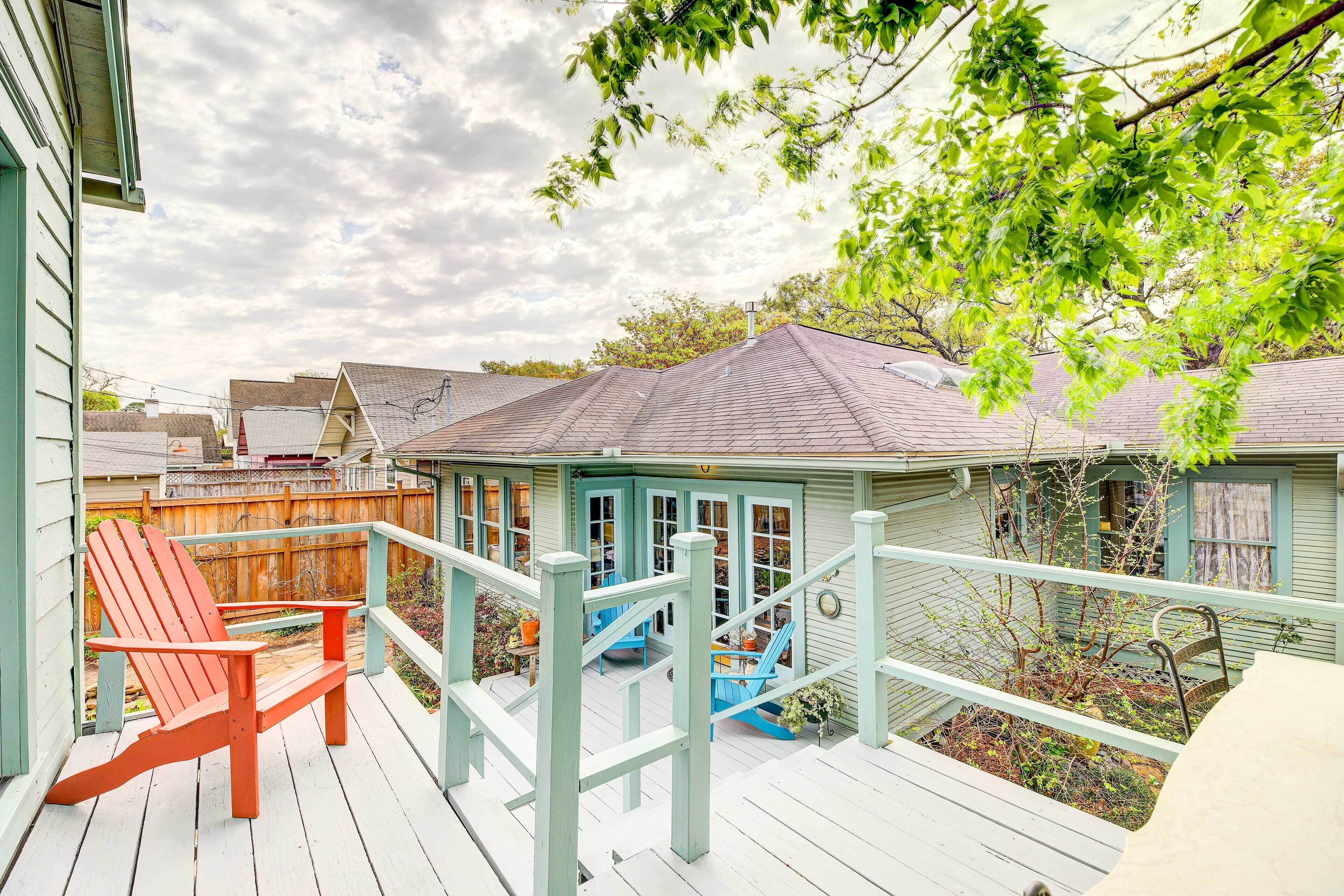 A wooden deck with a red Adirondack chair, a blue chair, and a small blue staircase leading to a covered area with windows.