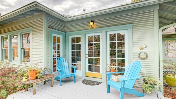 Une véranda avec deux fauteuils Adirondack bleus, un banc en bois et des plantes en pot.