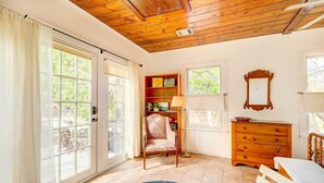 Une pièce avec un plafond en bois, une grande fenêtre, une chaise, une commode et un tapis.