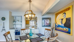 Zona pranzo con tavolo in vetro, sedie e lampadario. In secondo piano, si vede una cucina con lavello e pensili.