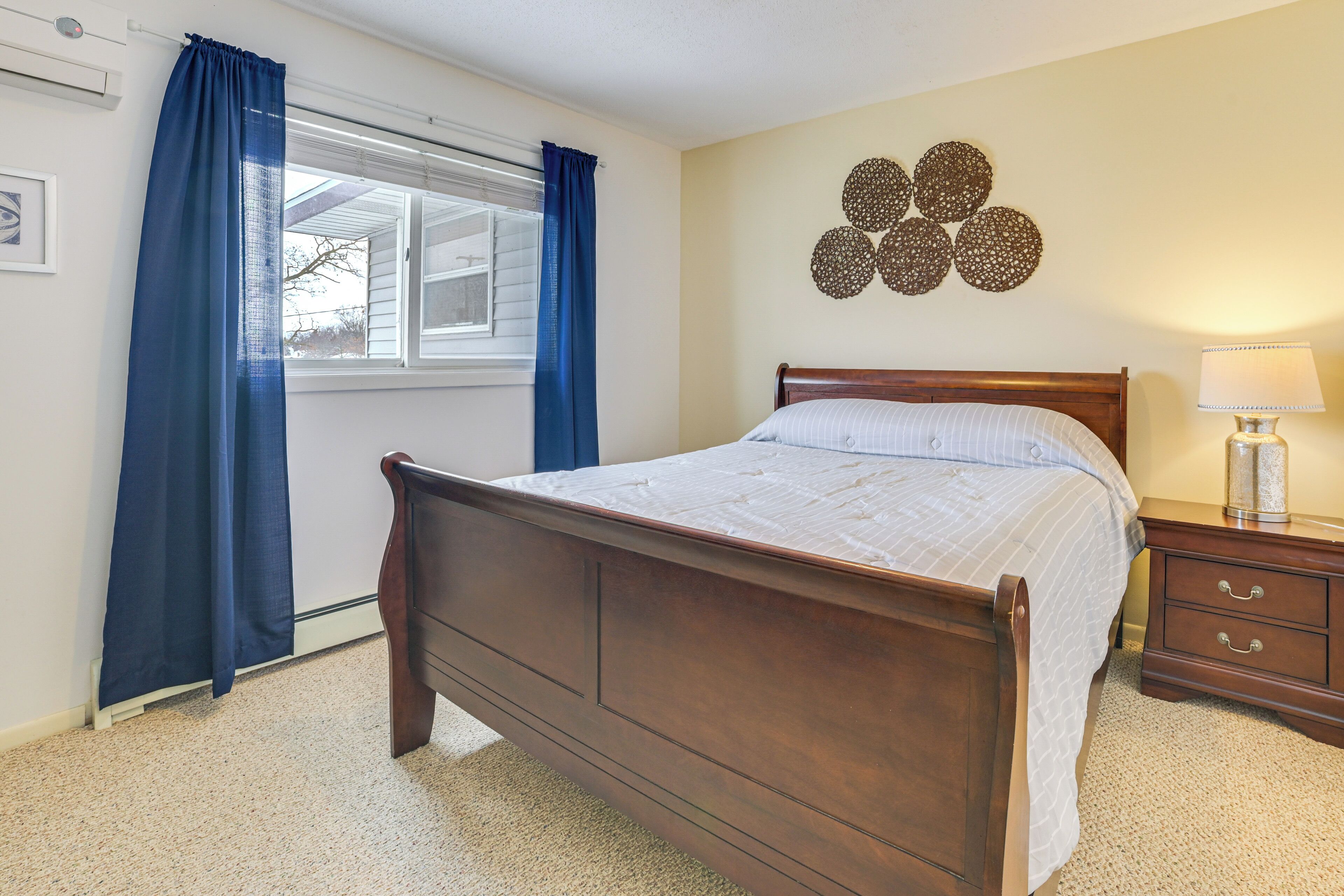 A bedroom with a wooden bed, a nightstand with a lamp, a window with curtains, and a wall decoration.