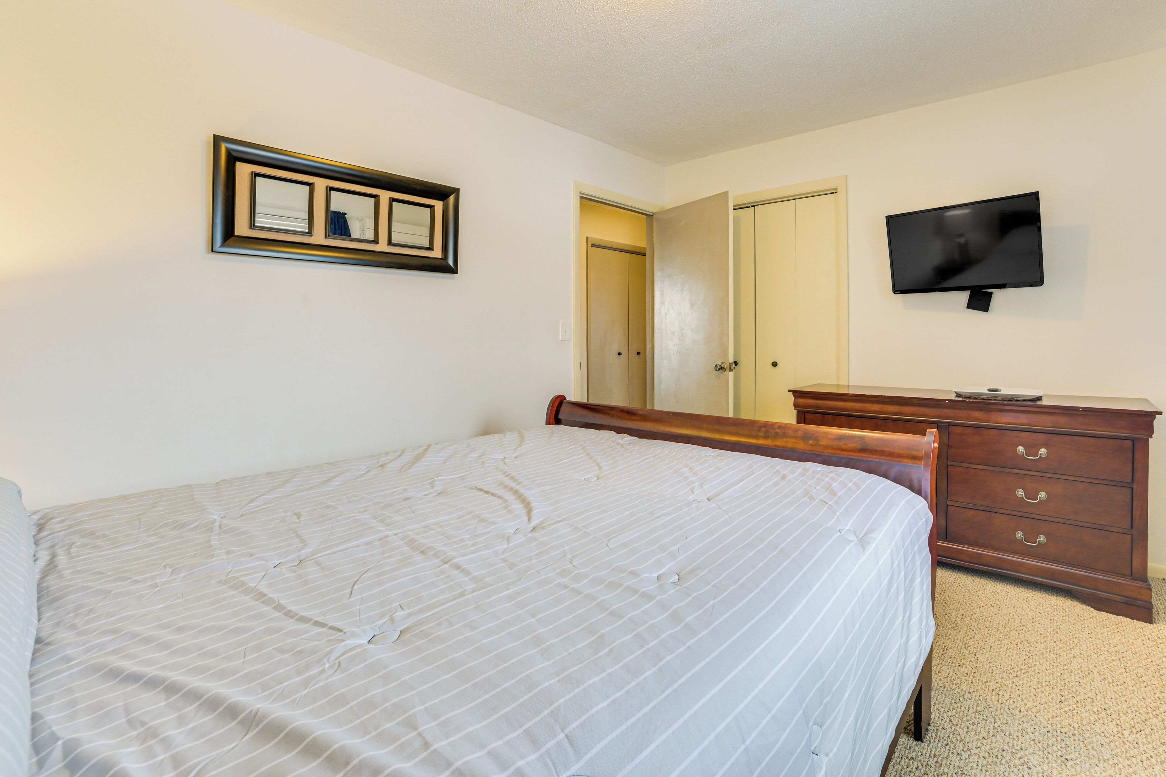 A bedroom with a bed, a dresser, a television, and a door.
