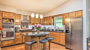 A kitchen with wooden cabinets, a stainless steel refrigerator, a built-in oven, and a central island with bar stools. - Family-friendly Brookville Home w/ Hot Tub! (Brookville)
