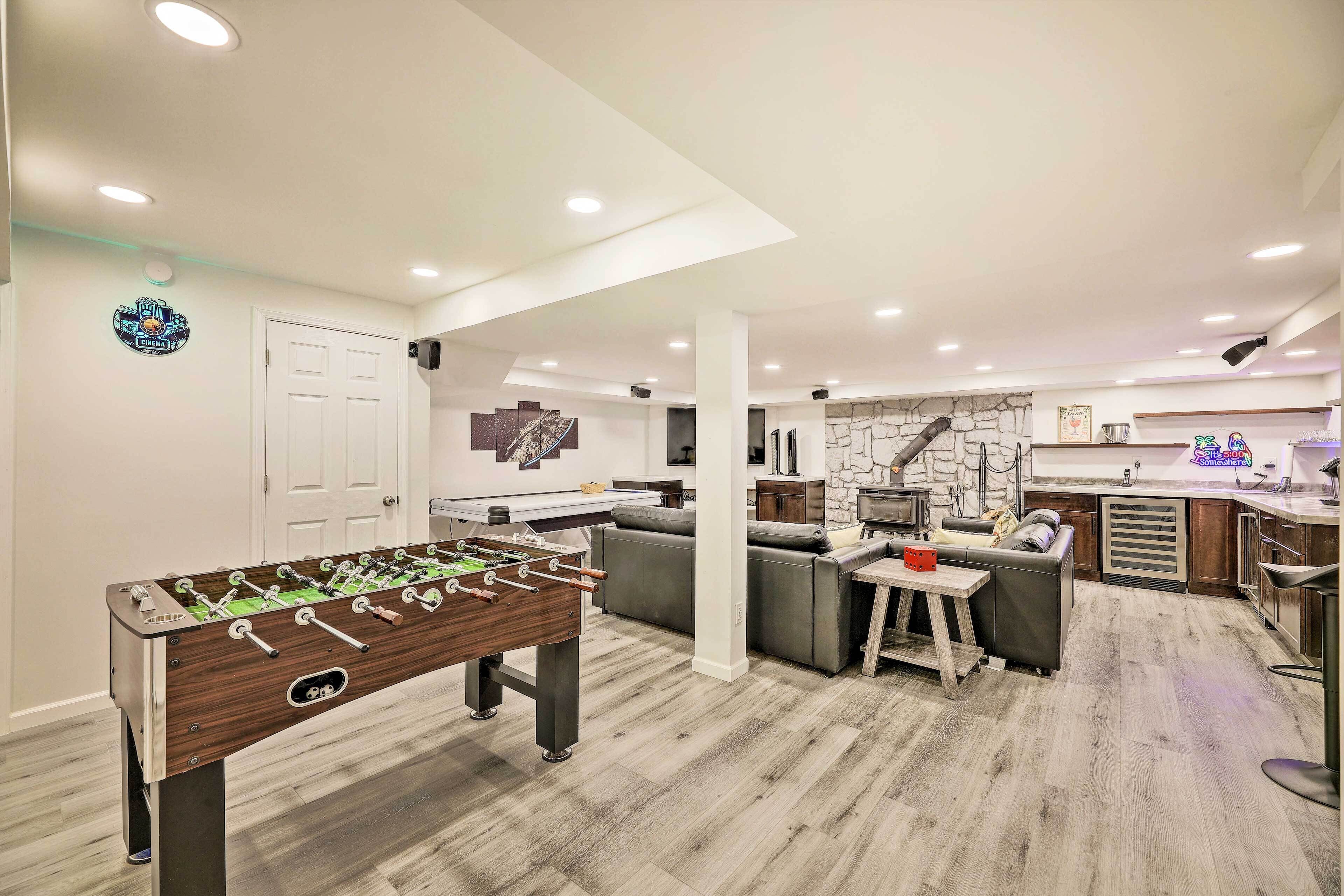 A spacious living area with a foosball table, a sofa, and a kitchen area with a stone backsplash.