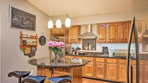 A kitchen with wooden cabinets, a central island with bar stools, a coffee-themed sign, and a hanging light fixture. - Family-friendly Brookville Home w/ Hot Tub! (Brookville)