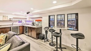 A modern kitchen with a bar area, a sofa, and a city view through the windows. - Family-friendly Brookville Home w/ Hot Tub! (Brookville)