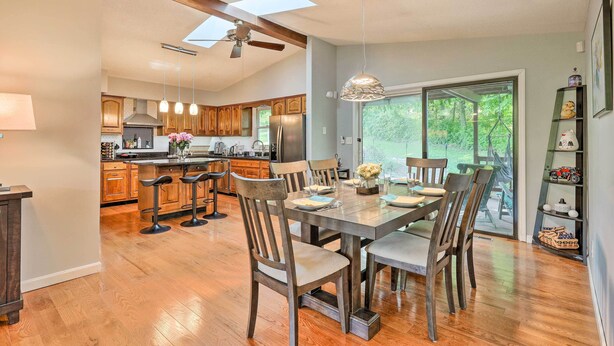 A spacious kitchen with wooden cabinets, a dining area with a large table and chairs, and a view of the outdoors through a sliding glass door. - Family-friendly Brookville Home w/ Hot Tub! (Brookville)