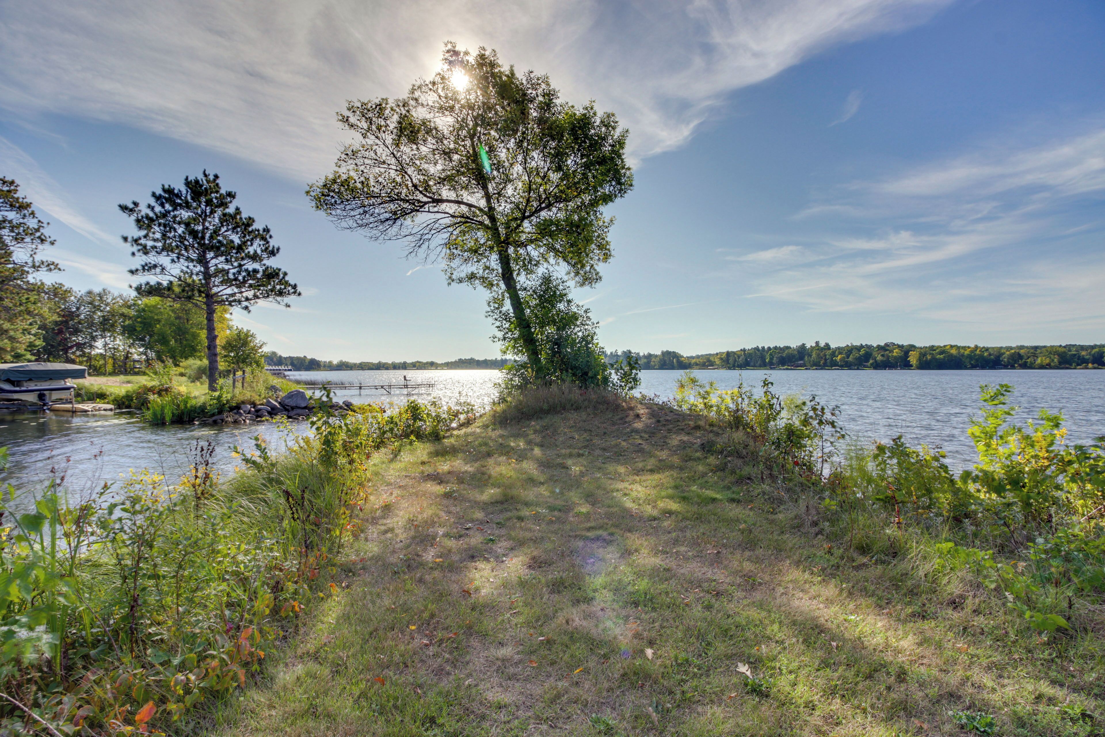 A lakeside path with a tree, grassy area, and a dock with boats.
