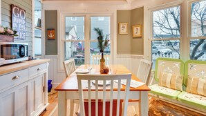A dining area with a wooden table, white chairs, and a green bench. - Historic Bemus Point Studio w/ Porch: Walk to Lake (Bemus Point)