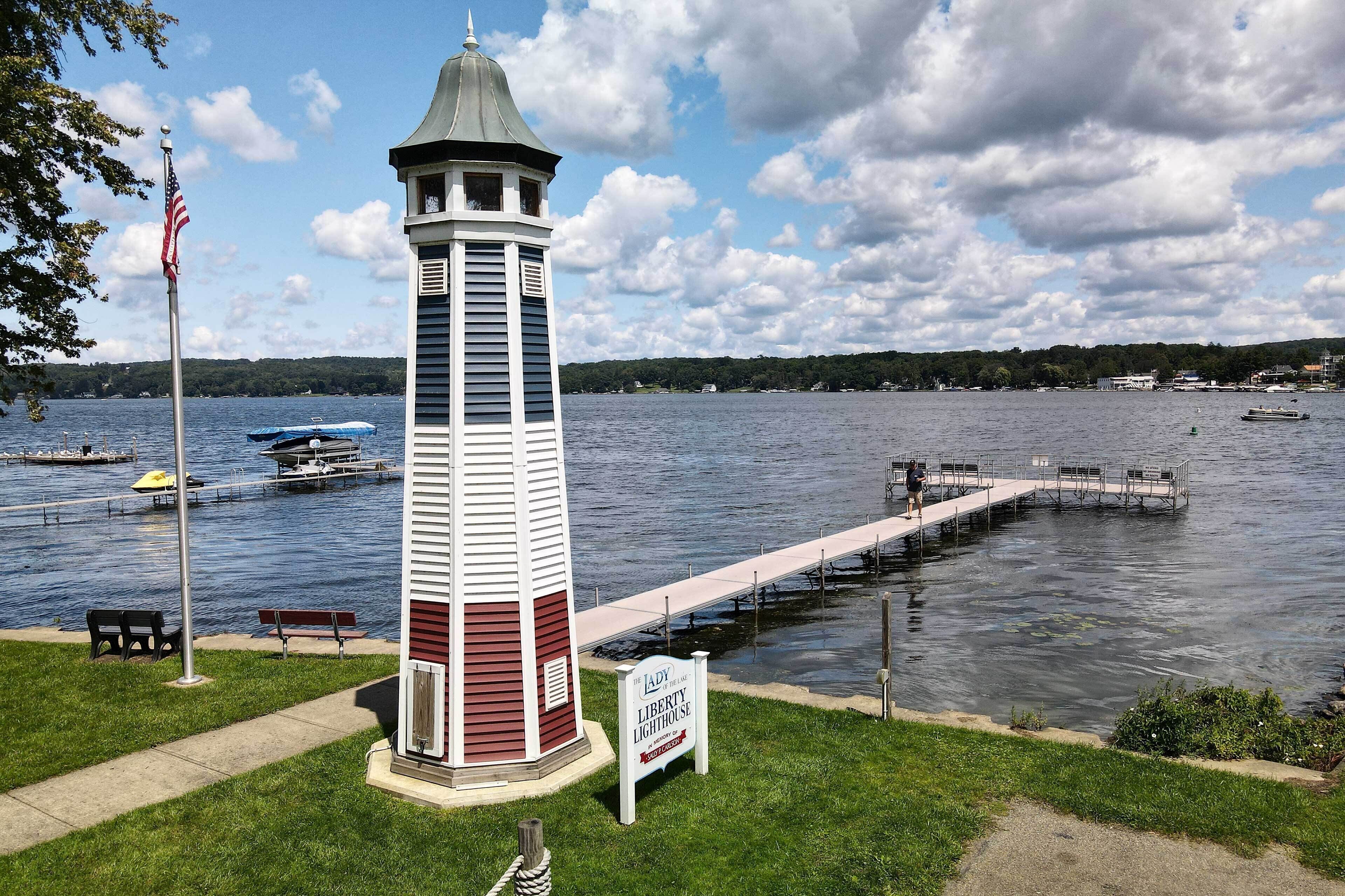 Un phare sur lequel on peut lire l’inscription « Phare de la Liberté », situé près d’un quai qui s’avance dans un lac, et entouré de zones herbeuses et de bancs.
