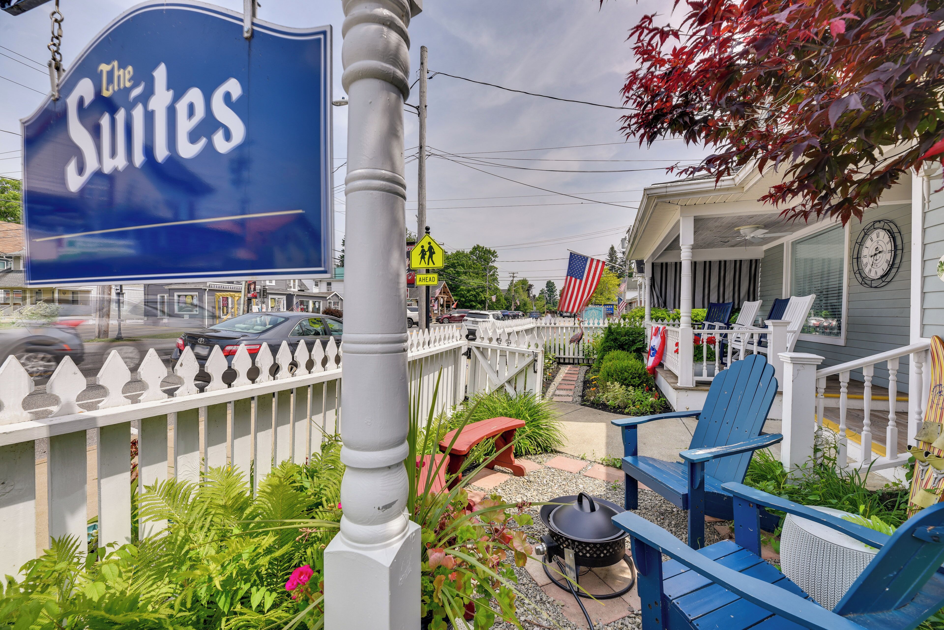 A sign for "The Suites" hotel, outdoor seating with blue chairs, a white picket fence, and an American flag.