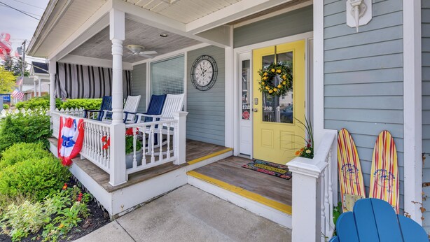 A porch with a white railing, a yellow door, and a clock on the wall. - Historic Bemus Point Studio w/ Porch: Walk to Lake (Bemus Point)