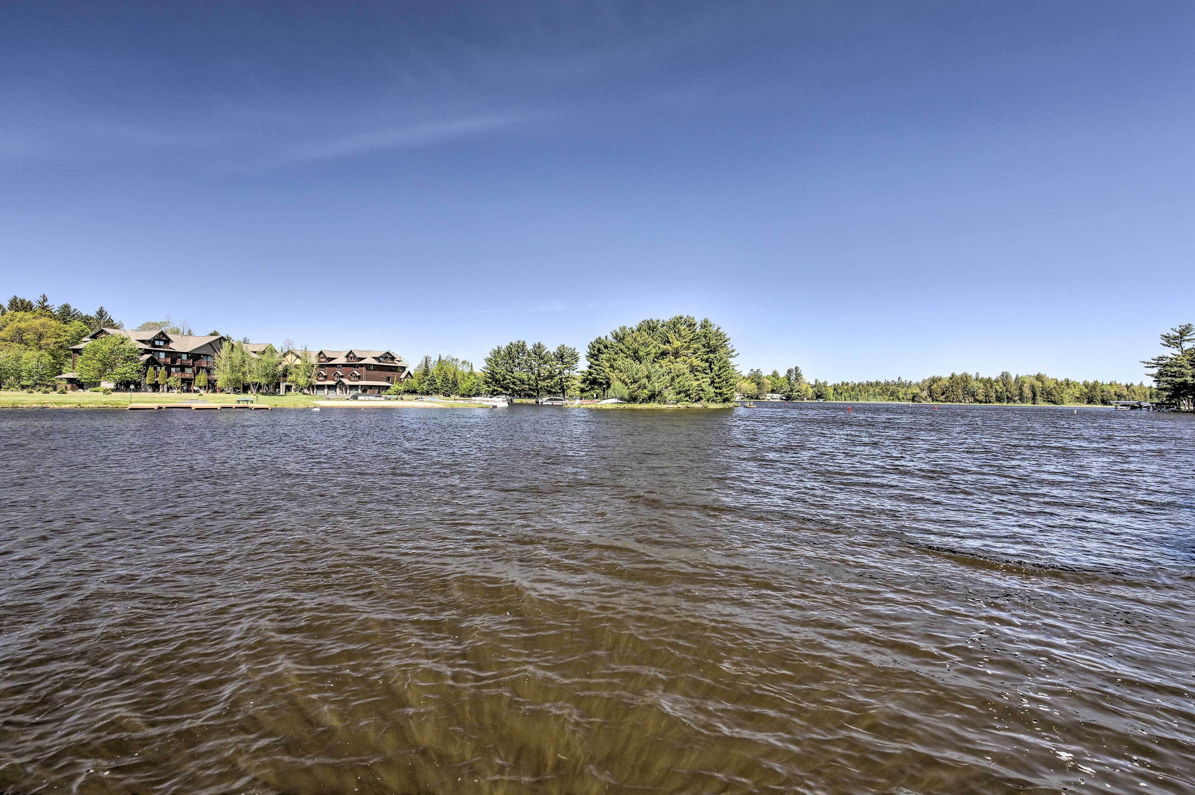 A lakeside view with a building featuring multiple stories and a prominent tree in the background.