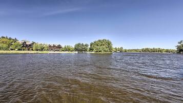 A lakeside view with a building featuring multiple stories and a prominent tree in the background.