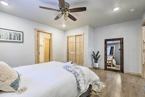 Quarto com cama, ventilador de teto, portas de madeira e um espelho refletindo um banheiro.