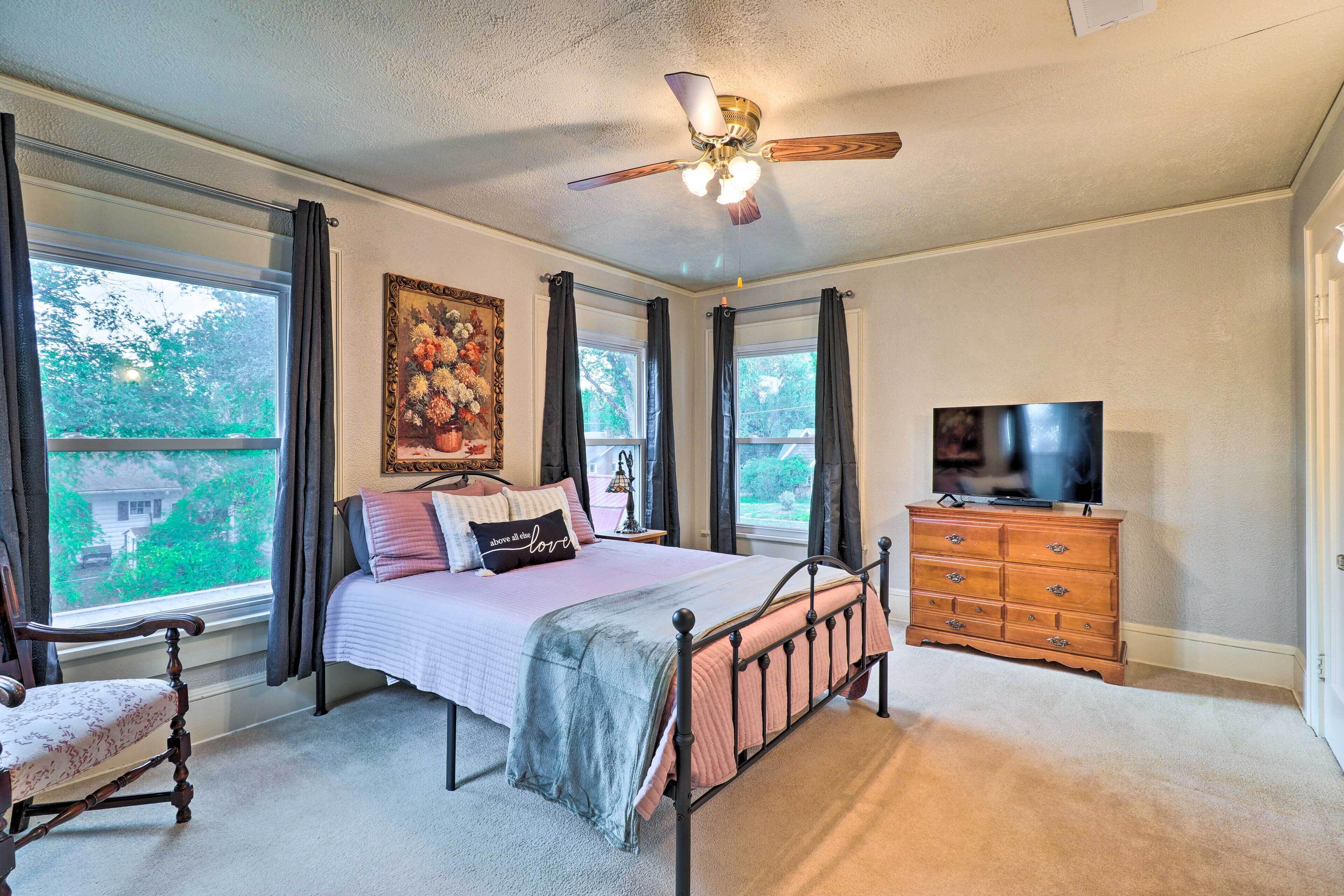 A bedroom with a bed, a dresser, a television, and a ceiling fan.