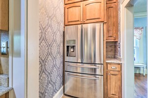 Un refrigerador de acero inoxidable con dispensador de agua, armarios de madera y un papel tapiz estampado en una cocina.