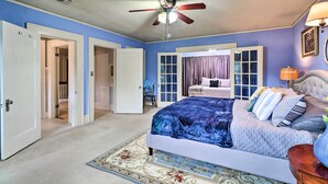 A bedroom with a bed, a ceiling fan, a window with curtains, and a door leading to another room.