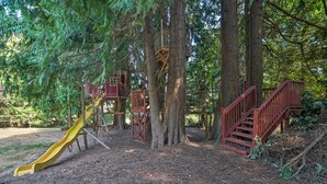 A playground with a yellow slide and red stairs, surrounded by tall trees. - Lovely Snohomish Studio Near Boating & Hiking (Snohomish)