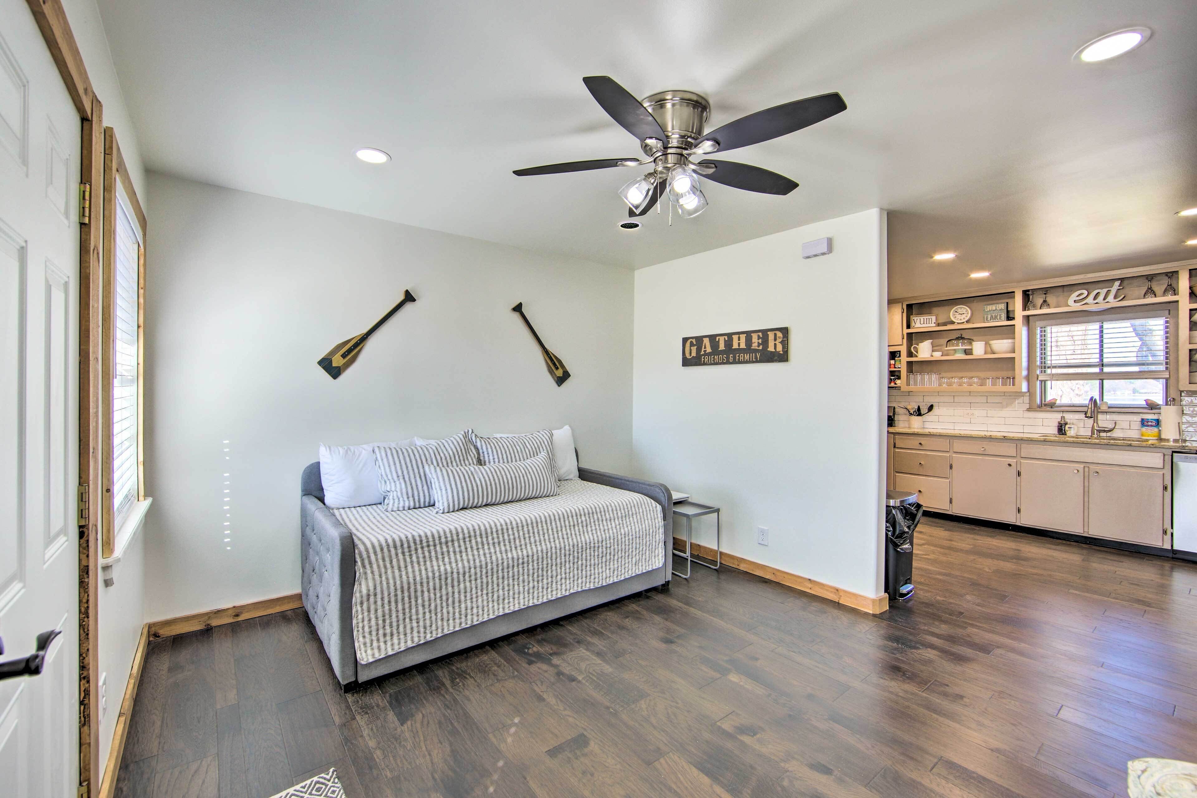 A bedroom with a bed, a ceiling fan, and a kitchen area with cabinets and a countertop.