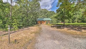 A gravel path leading to a rustic cabin with a green roof, surrounded by dense trees and a clear sky. - Heavenly Heber Springs Hideaway: Fish & Hike! (Heber Springs)