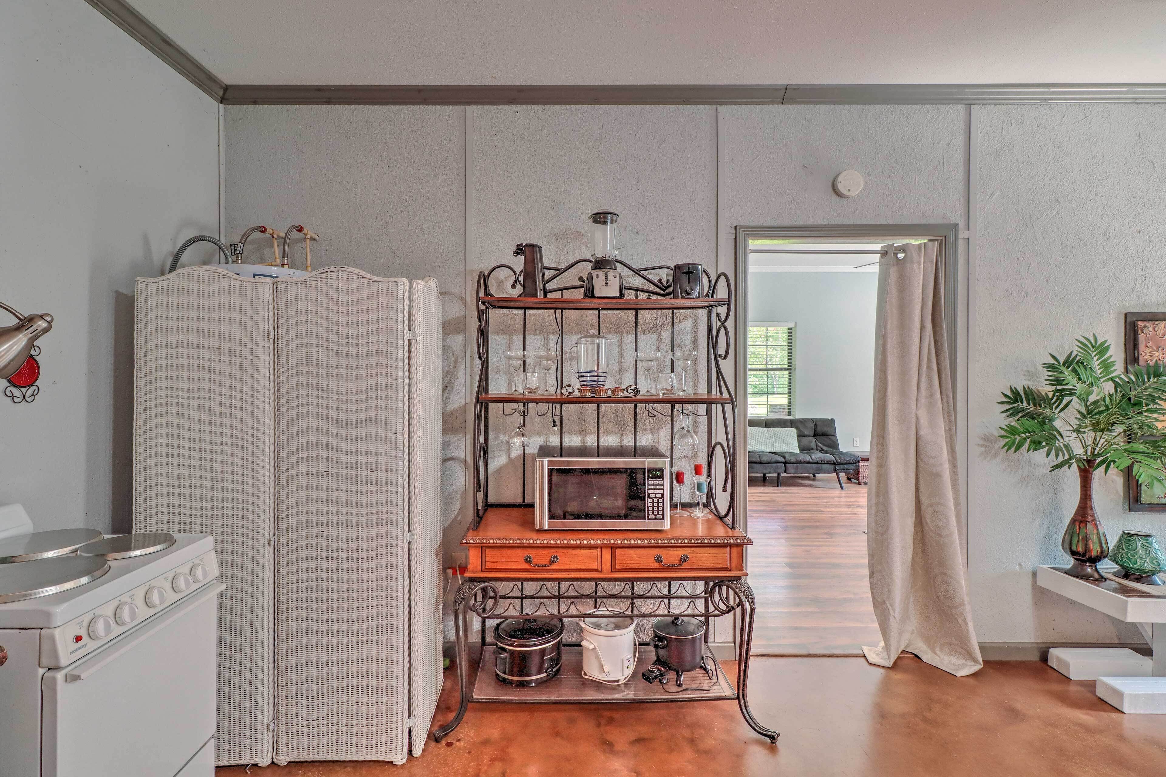Una cucina con un fornello, un mobiletto in vimini, un forno a microonde e una macchina da caffè su un supporto in legno.