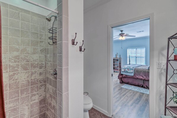 Un baño con ducha, inodoro y un pasillo que conduce a un dormitorio.