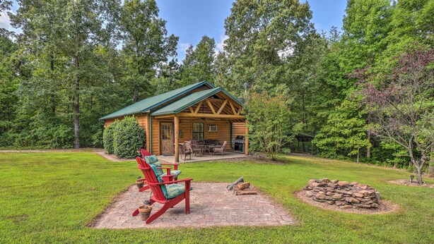 A log cabin with a green roof, surrounded by a grassy yard and trees. There is a fire pit and outdoor furniture. - Heavenly Heber Springs Hideaway: Fish & Hike! (Heber Springs)