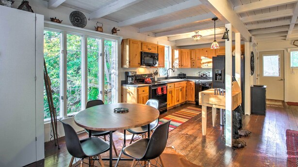 A spacious kitchen with wooden cabinets, a dining area with a round table and chairs, and a dog resting near the entrance. - Gilford Cabin - 2 Mi to Gunstock Mountain Resort! (Gilford)