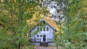 A two-story house with a front porch, surrounded by trees and a stone pathway. - Gilford Cabin - 2 Mi to Gunstock Mountain Resort! (Gilford)