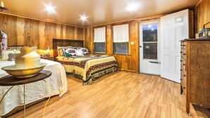 A cozy bedroom with wooden walls, a bed with a quilt, a bedside table with a lamp, and a dresser. - Historic Bruno 'hampton Creek Hideaway' on 2 Acres (Everton)