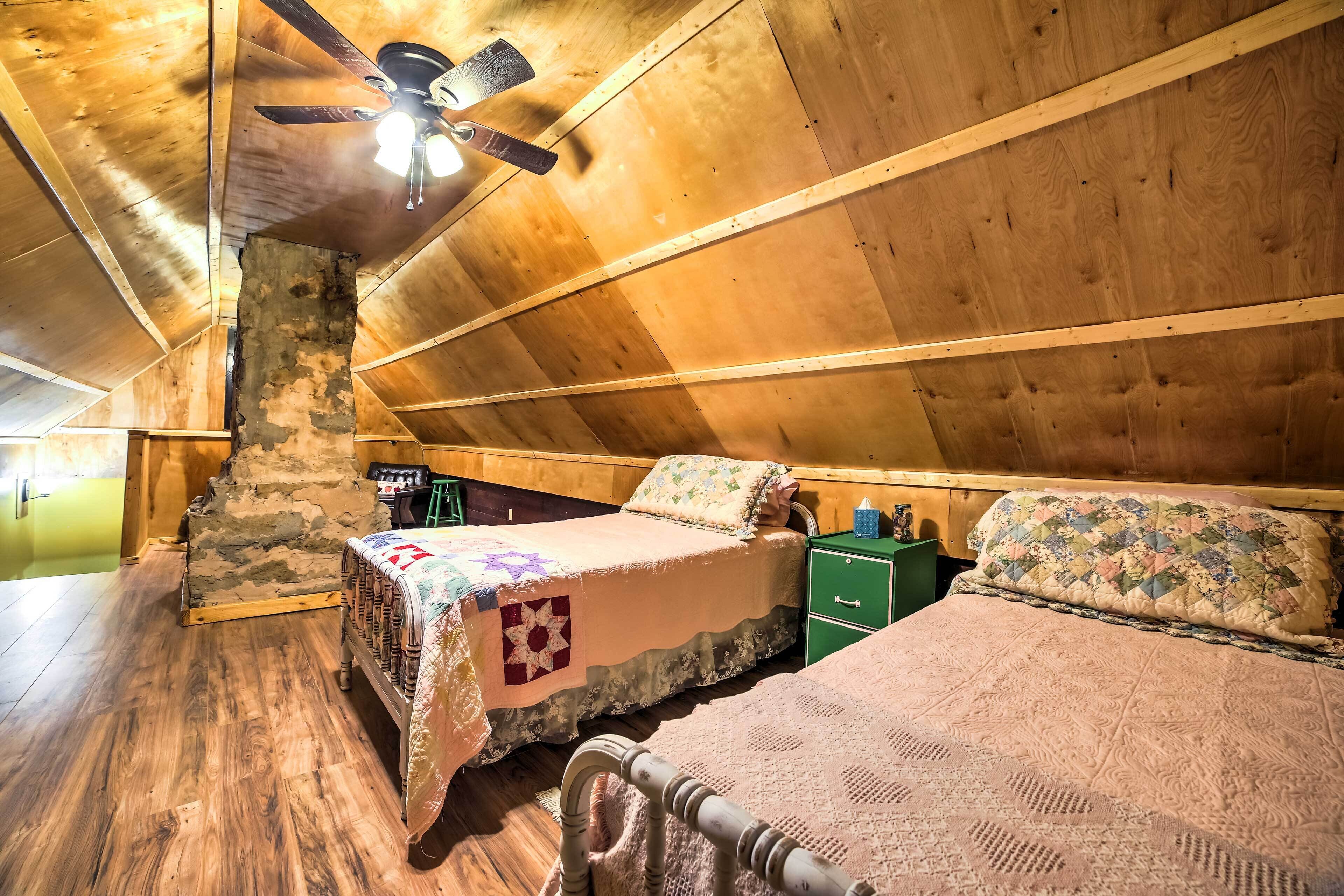 Un dormitorio acogedor en el ático con paredes de madera, techo inclinado, una cama con colcha estampada y una mesita de noche verde pequeña.