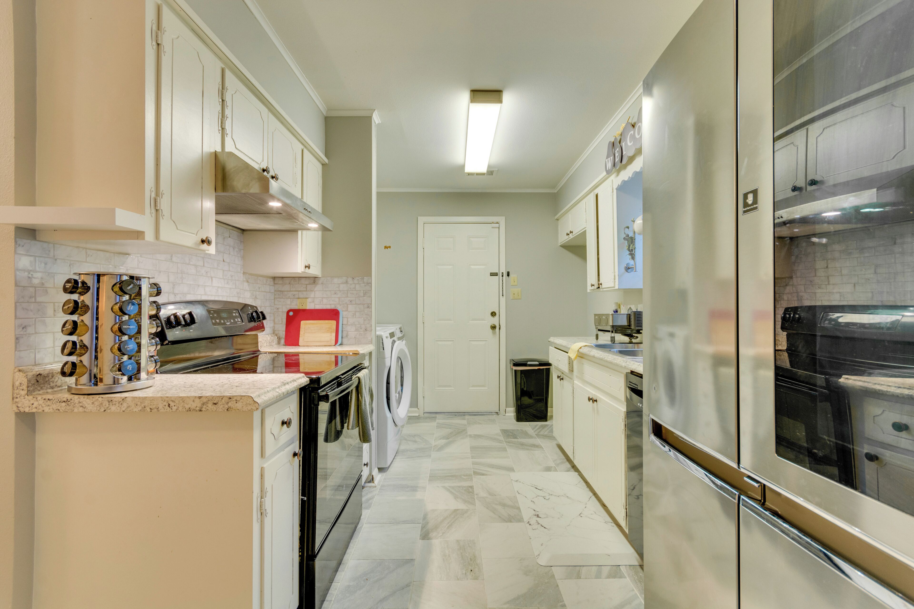A compact kitchen with white cabinets, a built-in oven, a washing machine, and a refrigerator.