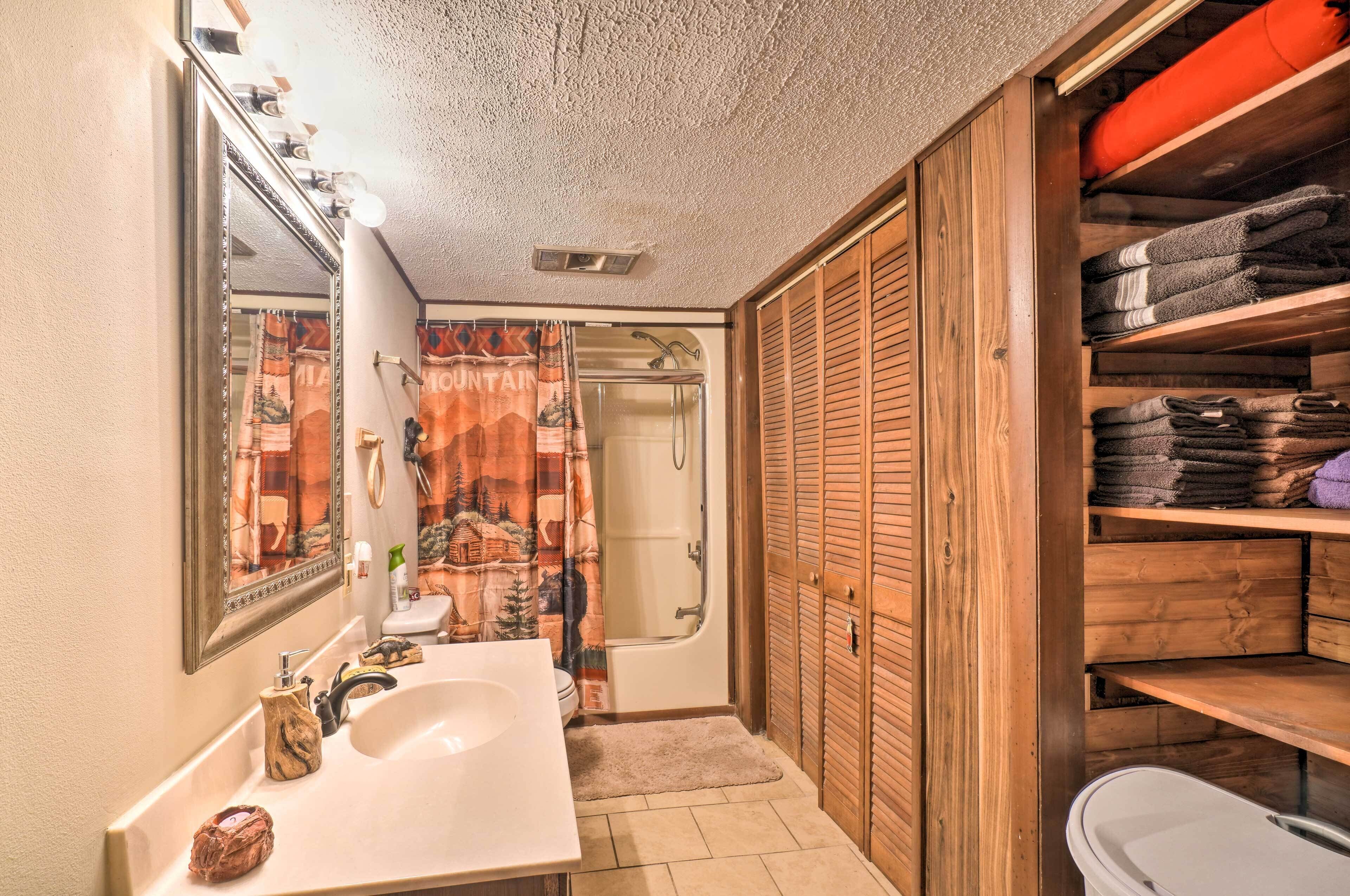 Ein Badezimmer mit Waschbecken, Spiegel, Dusche und Holzschrank mit gefalteten Handtüchern.