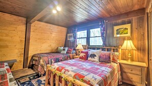 Un dormitorio acogedor de estilo cabaña con dos camas, paredes de madera, un ventanal grande y una lámpara en una mesita de noche.