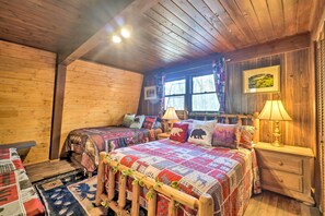 Un dormitorio acogedor de estilo cabaña con dos camas, paredes de madera, un ventanal grande y una lámpara en una mesita de noche.
